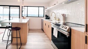 Une cuisine moderne dotée d’un grand îlot central, de tabourets de bar, d’une cuisinière et offrant une vue dégagée grâce à de grandes fenêtres.