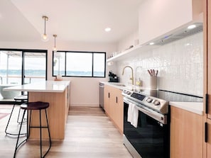 Una cocina moderna con una isla grande, taburetes de bar, una estufa y vistas amplias a través de grandes ventanales.