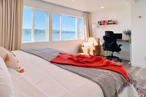 A bedroom with a bed, a desk, a chair, and a view of the water.