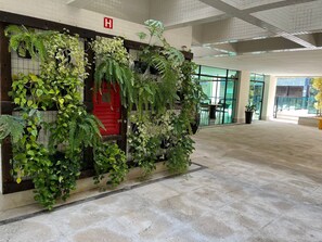 A hospital entrance with a red door, a tiled wall, and various green plants. - Riviera: M4 Giardino 44A, Beach front (Bertioga)