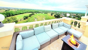 Een balkon met een rieten bank, een vuurkorf en uitzicht op een groen landschap.