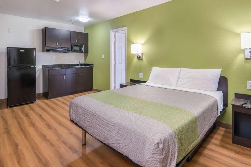 A hotel room with a bed, a kitchenette, and a door.