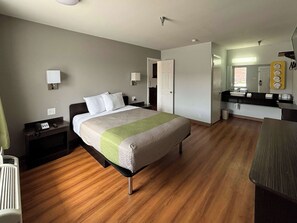 A hotel room with a bed, bedside table, lamp, and a bathroom with a sink and mirror. - Studio 6 Abilene, TX – East (Abilene)