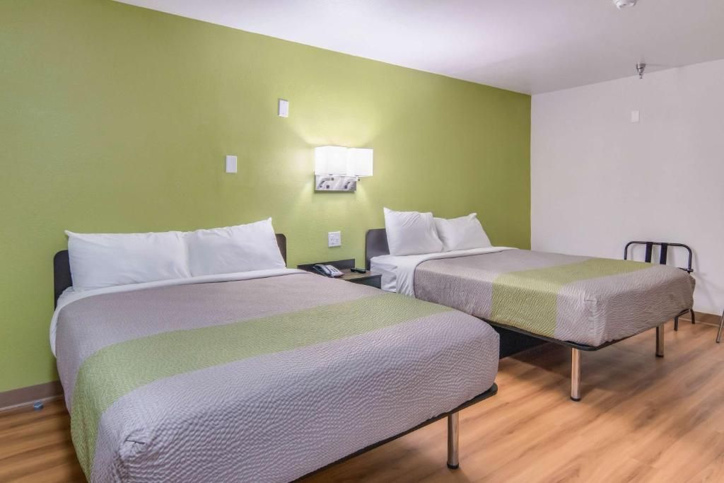 A hotel room with two beds, a nightstand, a lamp, and a chair.