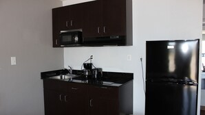 Una cocina compacta con armarios oscuros, un microondas, una estufa y un refrigerador negro.