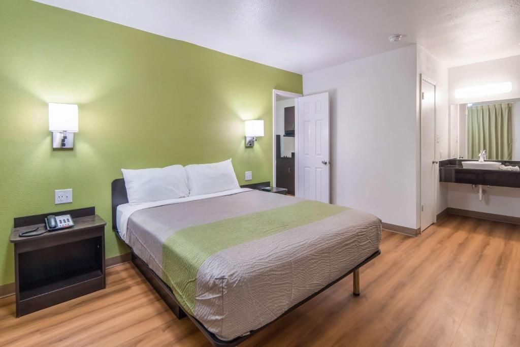 A hotel room with a bed, bedside table, lamp, and a bathroom with a mirror and sink.