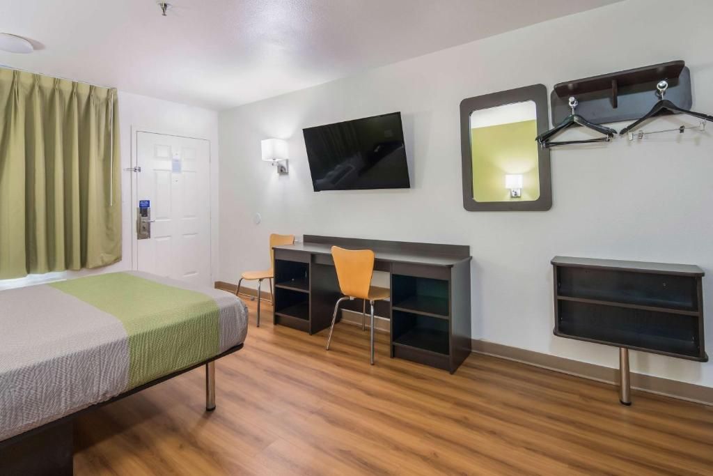 Een hotelkamer met een bed, bureau, stoel, televisie, spiegel en kapstok.