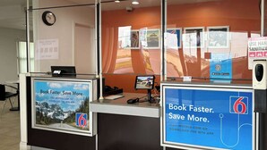 Un mostrador de recepción con una pantalla digital, un reloj y carteles promocionales para una aplicación móvil.