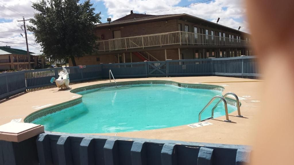 A swimming pool with a blue fence, a lifeguard chair, and a building in the background.