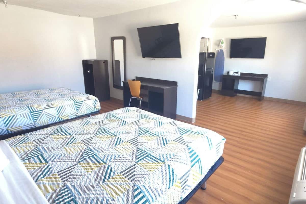 A hotel room with two beds, a desk, a chair, a TV, and a fireplace.
