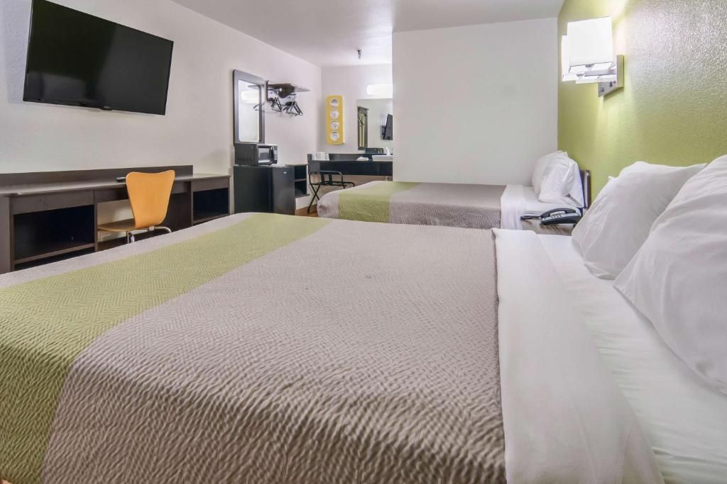 Habitación de hotel con dos camas, un escritorio, una silla, un televisor y un espejo.