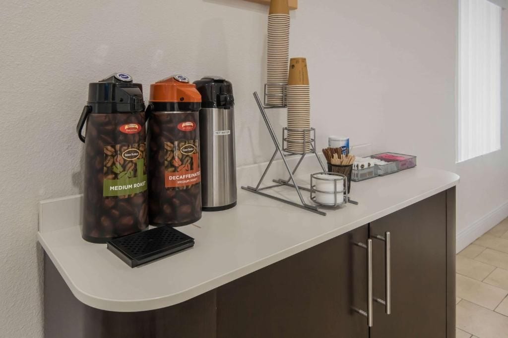 A coffee station with two coffee dispensers, a stack of paper cups, and a coffee pot on a counter.