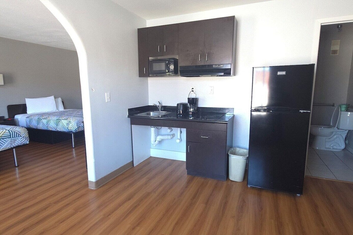 A compact hotel room with a kitchenette, two beds, a bathroom, and a door leading to another room.