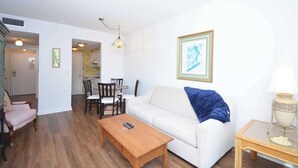 A living room with a white sofa, wooden coffee table, and a dining area with chairs and a table.