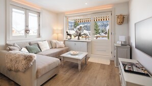 Un salon chaleureux avec un canapé, une table basse et une vue sur des montagnes enneigées, visible à travers une grande fenêtre.