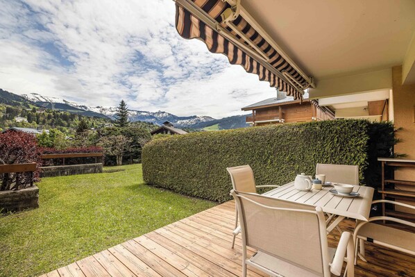 A patio with a table and chairs, a view of mountains, and a hedge. - Flat La Loge - At the foot of the Jaillet in Megève (Megève)