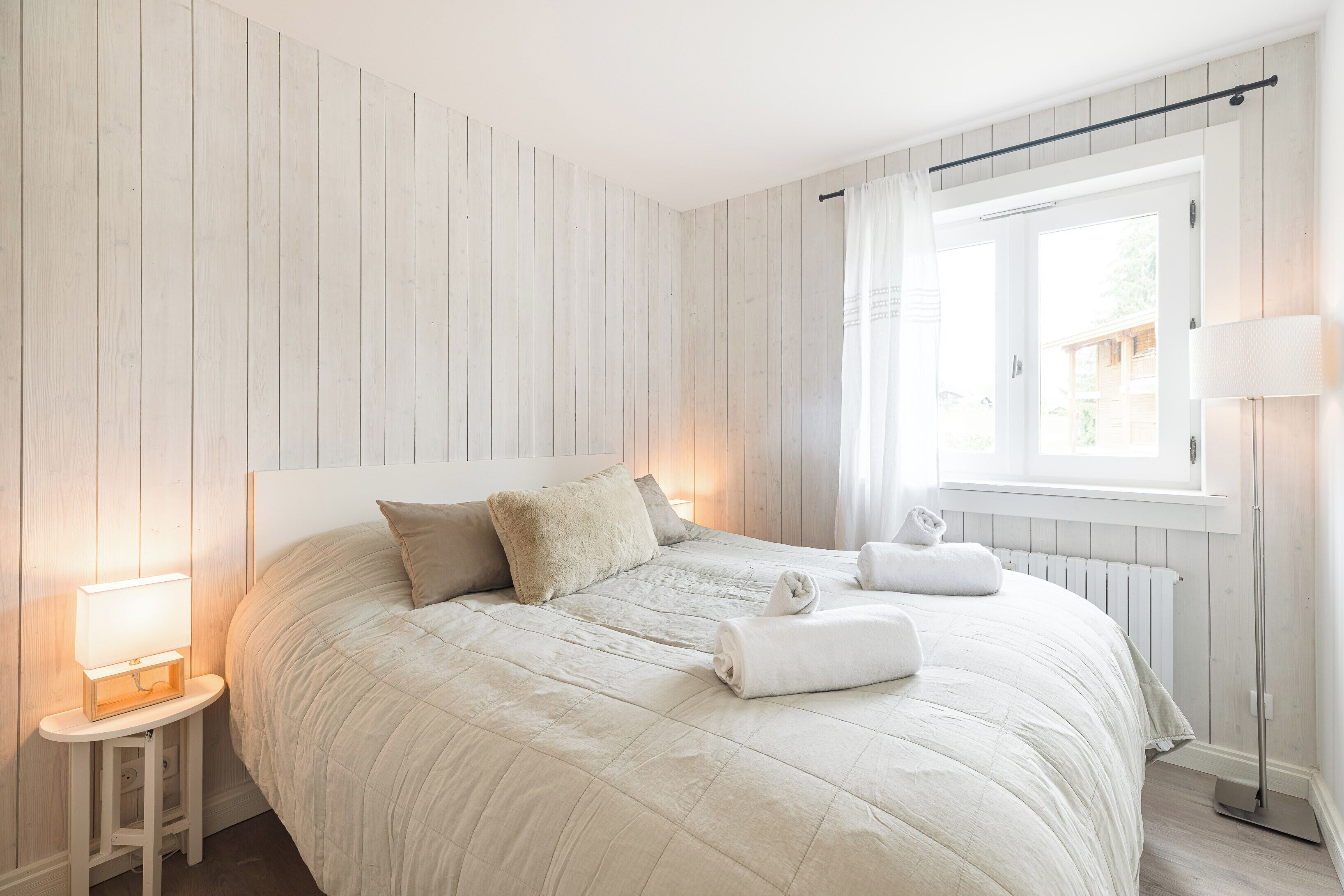 Un letto rifatto con coperta trapuntata, una lampada da comodino e un asciugamano arrotolato sul pavimento.