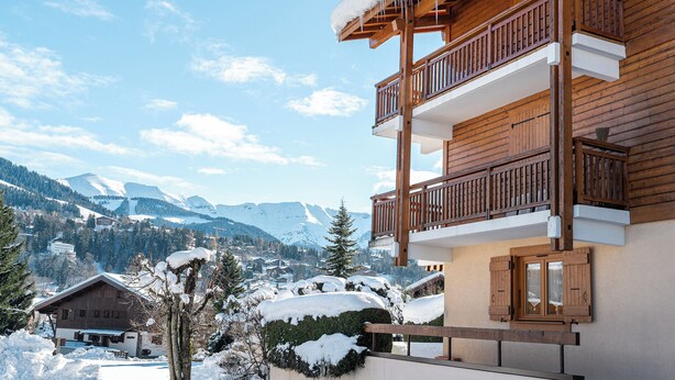 Un bâtiment en bois doté de balcons, entouré d’un paysage enneigé, avec une chaîne de montagnes en arrière-plan.