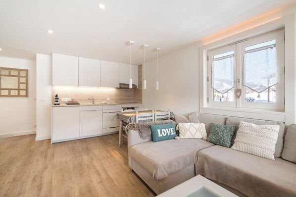 Un apartamento moderno con kitchenette, un sofá con cojines decorativos y una ventana con vistas.