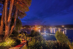 A lakeside view with a dock, trees, and a building with lights. - Woods End Landing (Bamfield)
