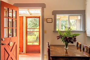A wooden door with glass panels, a dining table with chairs, a window with a view of greenery, and a framed picture on the wall. - Woods End Landing (Bamfield)