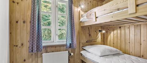 Een houten kamer met een stapelbed, een raam met gordijnen, een radiator en een bureau.