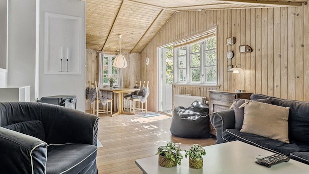 A cozy living room with a high wooden ceiling, a dining area with a table and chairs, and a large window with curtains. - 3 bedroom amazing home in Samsø (Samsø)