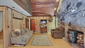 A cozy living room with a stone fireplace, wooden ceiling, and a television.