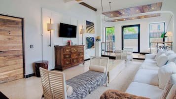 Una sala de estar con sofá, televisión, aparador de madera y un ventanal grande.