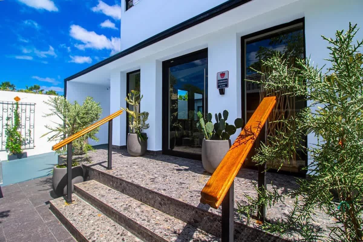 Un edificio con fachada blanca, una escalera de madera con barandilla amarilla y plantas en macetas.