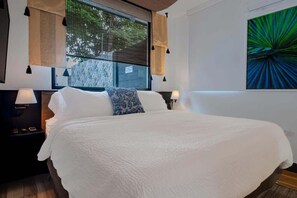 Un grand lit avec une literie blanche, une fenêtre avec des stores, une œuvre d’art accrochée au mur et des lampes de chevet.