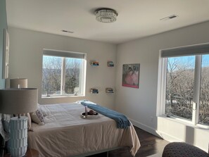 A bedroom with a bed, a lamp, a window, and a painting on the wall.