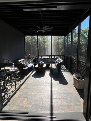 A covered outdoor seating area with a ceiling fan, a sofa, and a dining table.