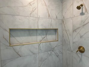 A bathroom with marble walls, a gold-framed shelf, and a gold shower handle.