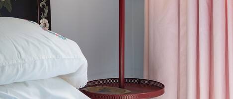 Un lit avec une literie blanche, une lampe de sol rouge et un mur orné d’œuvres d’art florales.