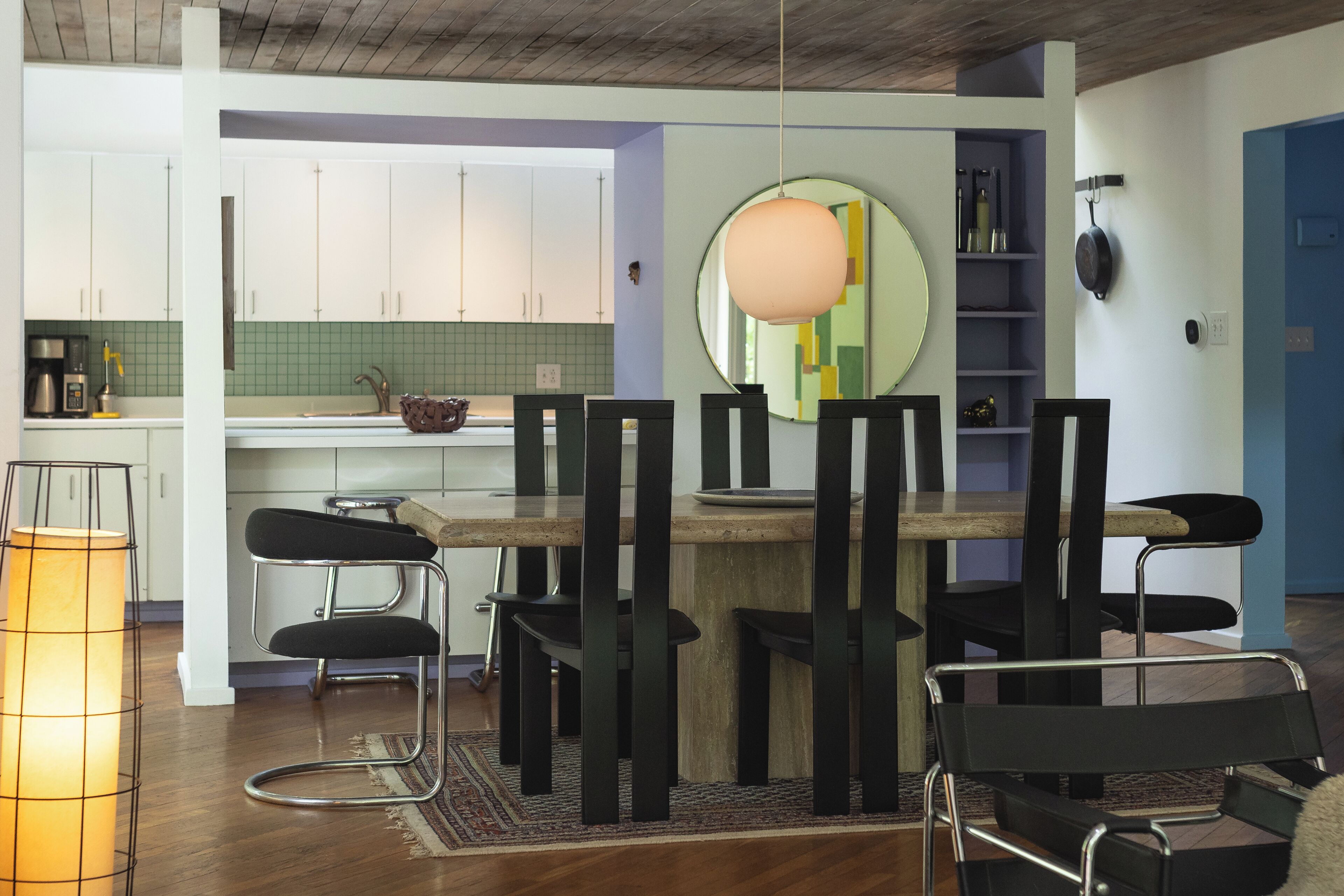 Une cuisine moderne avec des meubles blancs, une table à manger en bois, des chaises noires et un luminaire suspendu.