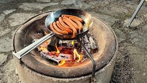 Ein tragbarer Grill mit Bratwürsten, die über offenen Flammen gegrillt werden.