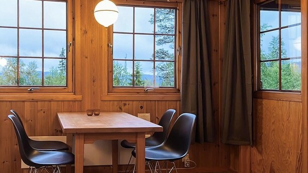 Ein Holzeinrichtung mit Tisch und Stühlen, große Fenster mit Vorhängen und einer hängenden Lampenleuchte.