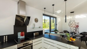 A modern kitchen with a black countertop, stainless steel appliances, and a glass dining table with a fruit bowl.