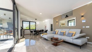 A modern living room with a grey sofa, a glass coffee table, and a dining area with a table and chairs.