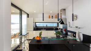 A modern kitchen with a large island, a view of the sea, and a dining area with a glass table.