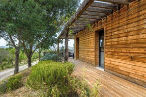 A wooden cabin with a covered porch, surrounded by trees and vegetation. - Lodge & piscine privée sur domaine viticole (Roquetaillade-et-Conilhac)