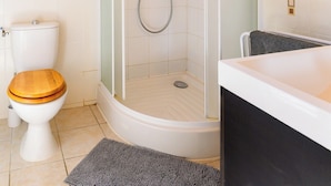 Un baño con ducha envuelta en vidrio, inodoro con asiento de madera y bañera.