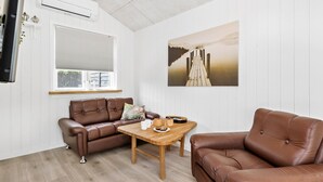 A room with a brown leather sofa, a wooden coffee table, and a painting of a pier. - 1 bedroom nice apartment in Skagen (Skagen)