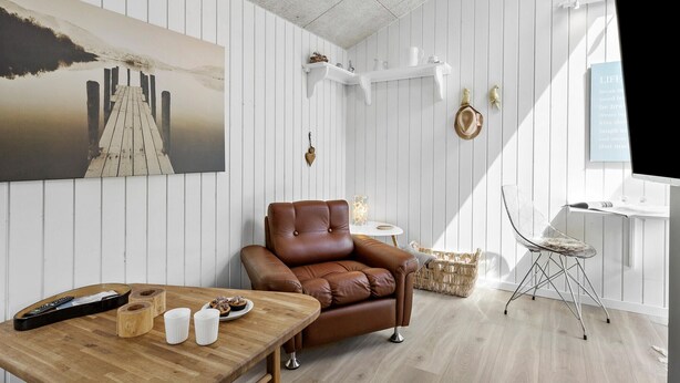 A cozy living room with a brown leather sofa, a wooden coffee table with a remote control, and a small side table with a lamp. - 1 bedroom nice apartment in Skagen (Skagen)