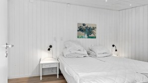 A bedroom with a white bed, a nightstand, a wall-mounted lamp, and a painting of flowers. - 1 bedroom nice apartment in Skagen (Skagen)