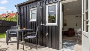 A wooden deck with a table and chairs, a door leading to an interior room with a sofa and a chair, and a window with a view of the outside. - 1 bedroom nice apartment in Skagen (Skagen)