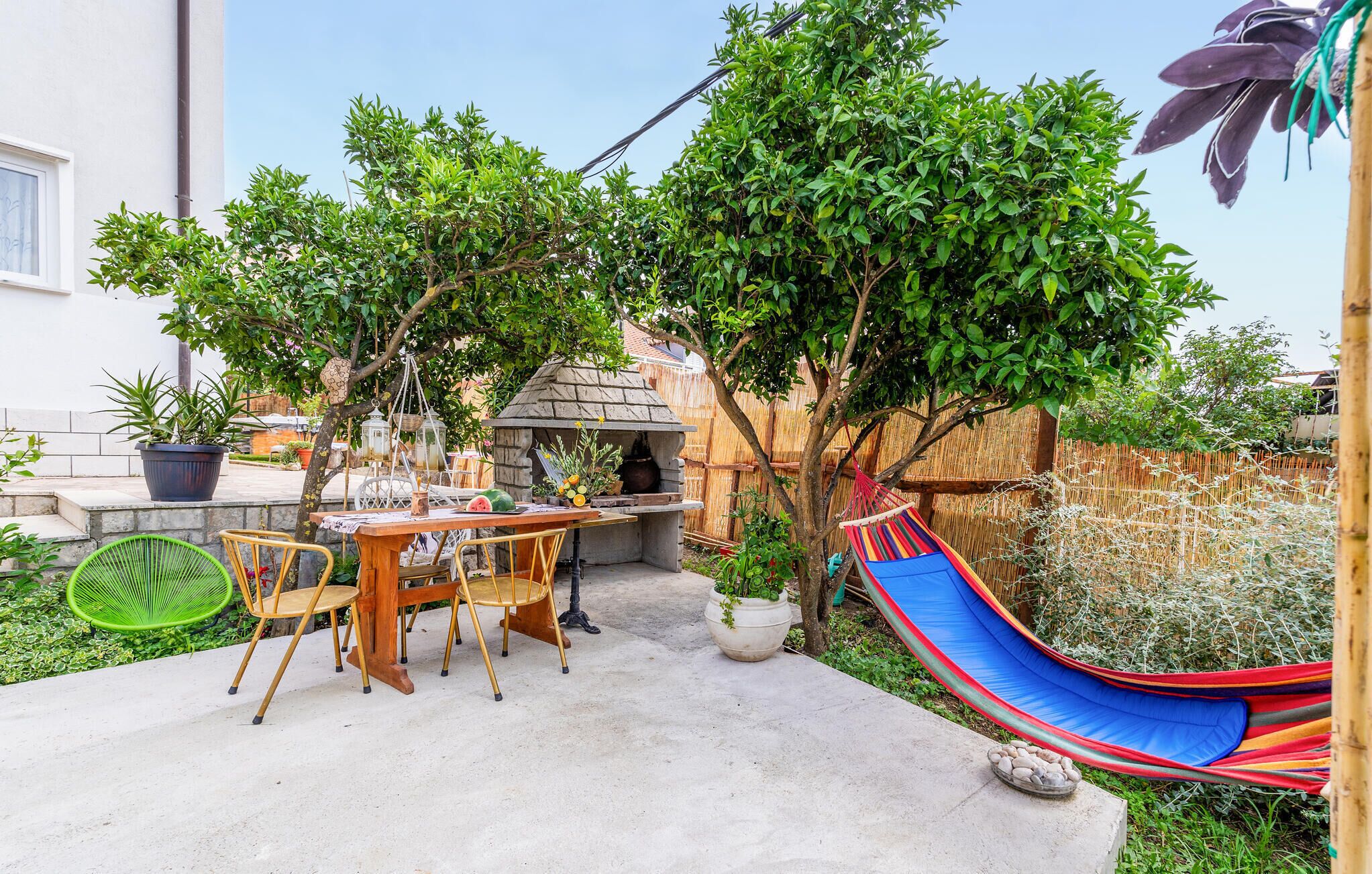 Une terrasse avec une table et des chaises, un hamac et un petit coin jardin agrémenté de plantes en pot.