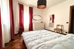 A bedroom with a large bed, a dresser, a chair, a small table, and a mirror on the wall.