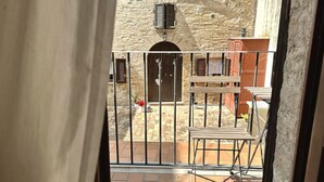 A balcony with a wrought iron railing, a stone building in the background, and a wooden table and chair. - R003 - Recanati, delightful three-room apartment in the center (Recanati)